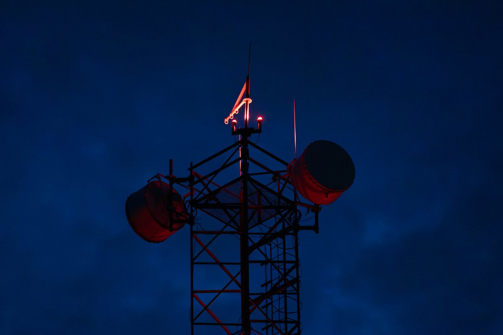 A transmission mast carrying red aviation lights at dusk